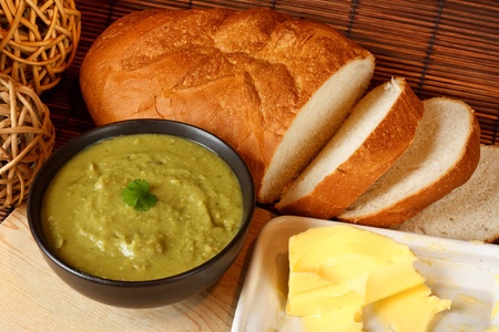 Bowl of homemade pea and ham soup in kitchen setting surrounded by crusty bread and butterの写真素材