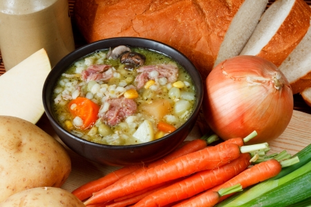 Bowl of ham broth in kitchen setting surrounded by ingredients, crusty bread and butterの写真素材