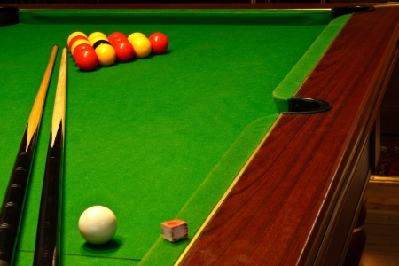 A green cloth billiards or pool table with english league red and yellow balls