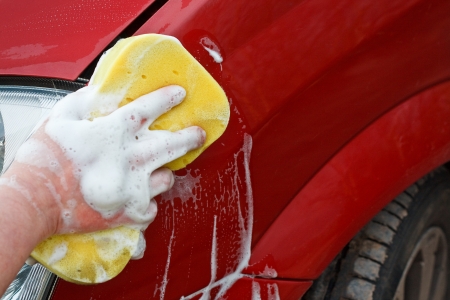 Washing the front wing of a car by hand with a yellow soapy spongeの写真素材