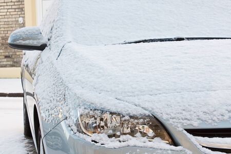 front bonnet and lights of european car covered in a layer of fresh snow during a harsh winter seasonの写真素材