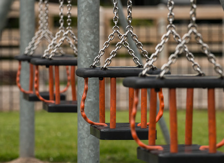 Row of swing seats at a local play park or children's playground provided by the local council for children to have fun in their community. Selective focus on a single Cradle seat.の写真素材
