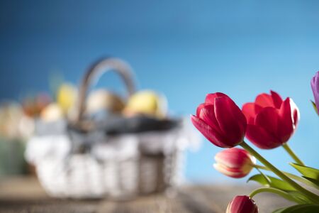 Easter theme. Bouquet of tulips. Easter eggs. Colorful bokeh, place for typography . Rustic wooden table. Blue background.の写真素材
