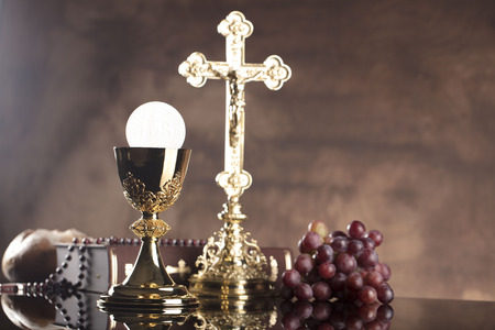 Catholic religion theme. Holy Bible, the cross and gold chalice on wooden table and stone background.の写真素材