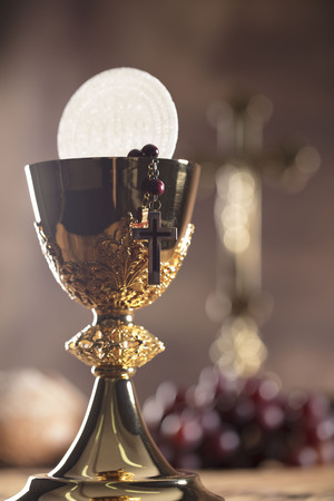 Catholic religion theme. Holy Bible, the cross and gold chalice on wooden table and stone background.の写真素材