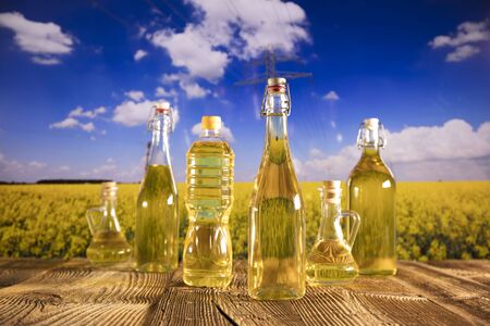 Rapeseed oil on rapeseed field background. Bottles with oil on rustic table. Summer time.の写真素材