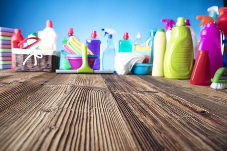 Spring cleanup theme. Variety of colorful house cleaning products on a rustic wooden table and blue background.の写真素材