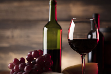Glass of red wine, cheese and grapes on old wooden table. Old wooden background.の写真素材