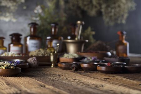 Natural medicine background. Brass mortar, bottles. Rustic table. Assorted dry herbs in bowls. Bokeh.の写真素材