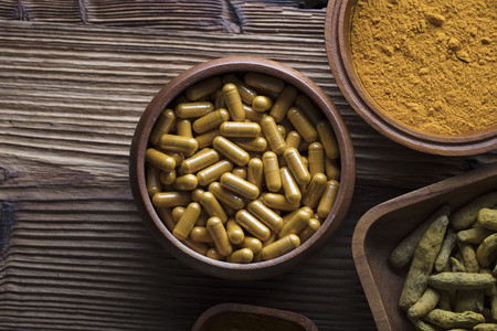 Curcuma capsules, turmeric roots and powder in bowls. Anti cancer medicine. Wooden table. Top view shot.の写真素材