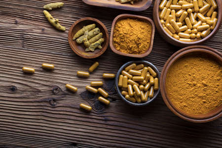Curcuma capsules, turmeric roots and powder in bowls. Anti cancer medicine. Wooden table. Top view shot.の写真素材