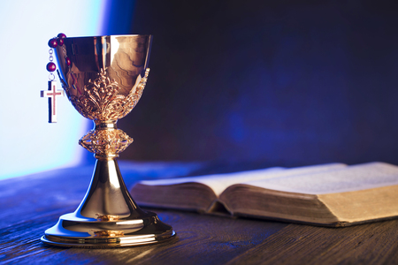 Roman Catholic Church theme. The Cross, Holy Bible and golden chalice on brown wooden table.の写真素材