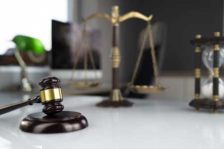 Law concept background. Gavel, scale and hourglass on the white glass table in the lawyer office.の写真素材