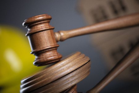 Construction law concept. Wooden gavel on the gray background with the house model and the yellow hardhat.の写真素材