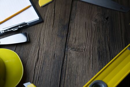 Contractor concept. Tools of the contractor : yellow hardhat, libella and hand saw on the rustic...