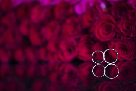 Romantic day concept. Wedding rings lying on shining table on the red roses background.の写真素材