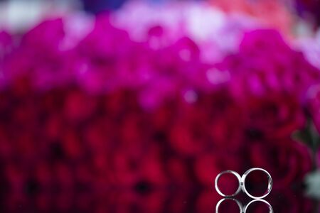 Romantic day concept. Wedding rings lying on shining table on the red roses background.の写真素材
