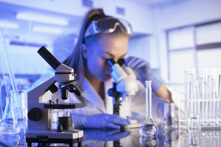 Laboratory interior. Science research concept. Young scientist during experiment and using microscope in modern laboratory. Glass tubes and beakers.の写真素材