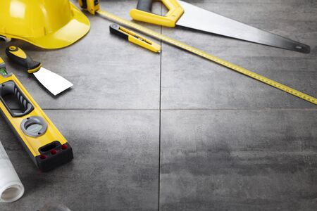Contractor concept. Tool kit of the contractor: yellow hardhat, libella, hand saw. Plans and notebook on the gray tiles background.の写真素材