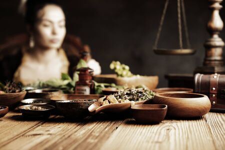 Natural medicine concept. Vintage pharmacist preparing natural medicament. Brass mortar and  bottles. Rustic table. Assorted dry herbs in bowls.の写真素材