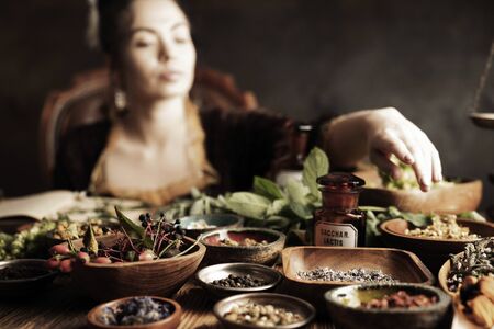 Natural medicine concept. Vintage pharmacist preparing natural medicament. Brass mortar and  bottles. Rustic table. Assorted dry herbs in bowls.の写真素材
