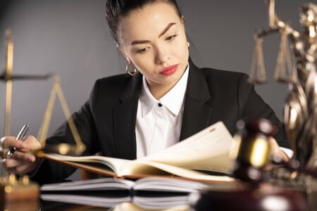 Young female lawyer during work in chamber. Gavel, scale and Themis statue on the brown table.の写真素材