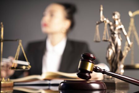 Young female lawyer during work in chamber. Gavel, scale and Themis statue on the brown table.の写真素材