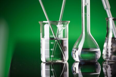 Coronavirus pandemic theme. Science research concerning fast covid tests and anti-covid vaccine. Beakers and test tubes on green background in laboratory.の写真素材