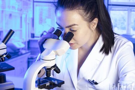 Science research concept. Young scientist during experiment and using microscope in modern...