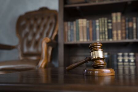 Judge office. Gavel on brown shining table and collection of legal books in the bookshelf.の写真素材