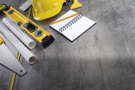 Contractor concept. Tool kit of the contractor: yellow hardhat, libella, hand saw. Plans and...