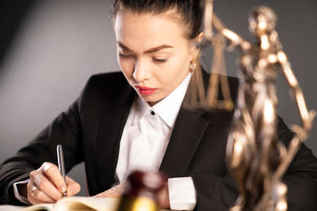Young female lawyer during work in chamber. Gavel, Themis statue and scale on the brown shining...