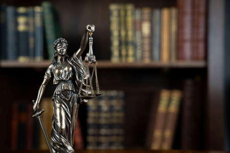 Law theme. Judge chamber. Themis statue on brown shining desk. Collection of legal books in the bookshelf.の写真素材