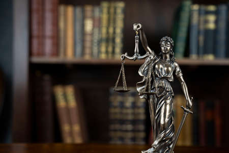Law theme. Judge chamber. Themis statue on brown shining desk. Collection of legal books in the bookshelf.の写真素材