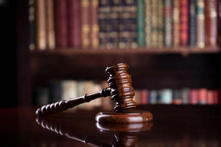 Judgeâ€˜s gavel on brown shining table and bookshelf background. Law and justice concept.