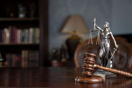 Law theme. Judge chamber. Themis, gavel and scale on brown shining desk. Collection of legal books...