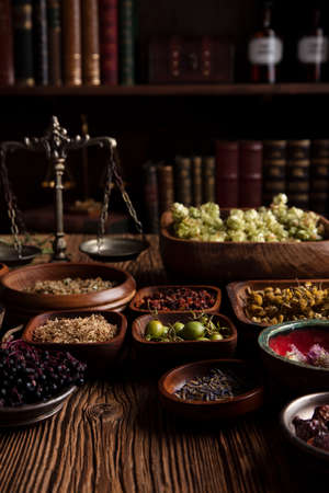 Natural medicine theme. Assorted dry herbs in bowls and brass mortar on rustic wooden table.の写真素材