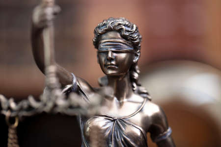 Law and justice concept. Themis sculpture in lawyers office. Bookshelf with legal books in background.の写真素材