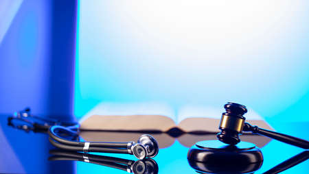 Medical law concept. Gavel, legal code and stethoscope on the glass table. Blue light.の写真素材