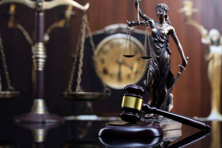 Law concept. Judge wooden gavel, scale, old clock and Themis statue on brown background.の写真素材