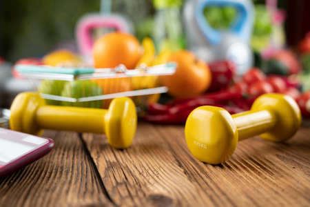 Fitness concept. Healthy nutrition: fruits and vegetables. Equipment for fitness exercises: weighing machine and dumbbells.の写真素材