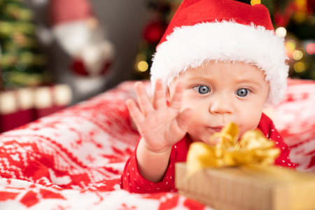 Christmas time. Beautiful little baby boy dressed as Santa celebrates Christmas. Bokeh background.の写真素材