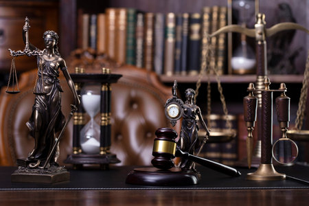 Law and justice theme. Judge chamber. Themis statue, gavel and scale on brown desk. Legal books in the bookshelf as background.の写真素材