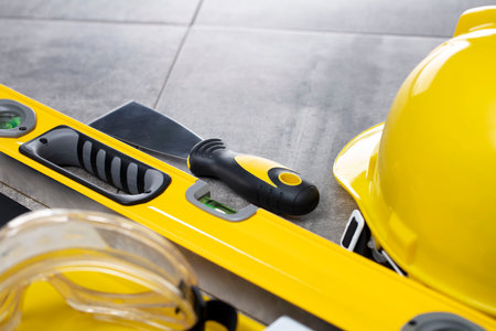 Contractor concept. Tool kit of the contractor: yellow hardhat, libella and tools on the gray tiles...