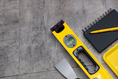 Contractor concept. Tool kit of the contractor: yellow hardhat, libella and tools on the gray tiles...