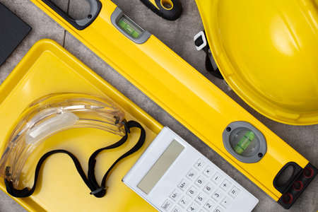 Contractor concept. Tool kit of the contractor: yellow hardhat, libella and tools on the gray tiles...