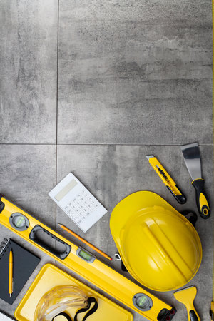Contractor concept. Tool kit of the contractor: yellow hardhat, libella and tools on the gray tiles...