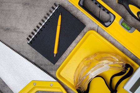 Contractor concept. Tool kit of the contractor: yellow hardhat, libella and tools on the gray tiles background.の写真素材