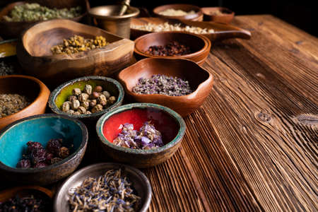 Natural medicine background. Assorted dry herbs in bowls and brass mortar on rustic wooden table.