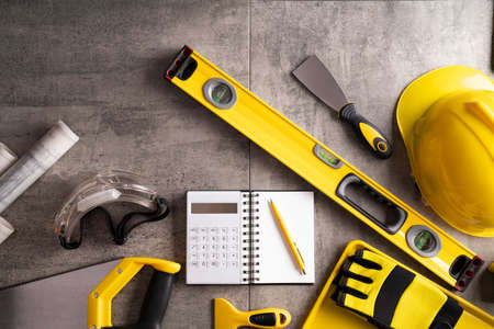 Contractor theme. Tool kit of the contractor: yellow hardhat, libella and tools on the gray tiles background.の写真素材